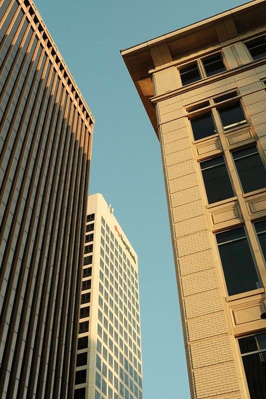 Three tall buildings with modern architecture against a clear blue sky, viewed from a low angle
